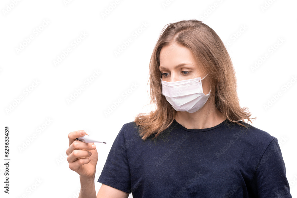 Young woman in protective mask standing against white background and measuring temperature using electronic thermometer Young woman in protective mask standing against white background and measuring temperature using electronic thermometer