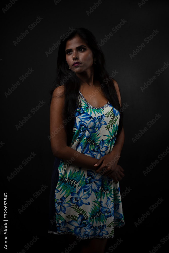 Fashion portrait of a dark skinned young Indian/African girl in western floral dress in front of a dark copy space studio background. Indian lifestyle. Fashion portrait of a dark skinned young Indian/African girl in western floral dress in front of a dark copy space studio background. Indian lifestyle.