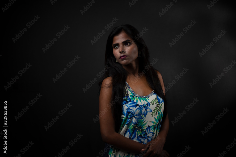 Fashion portrait of a dark skinned young Indian/African girl in western floral dress in front of a dark copy space studio background. Indian lifestyle. Fashion portrait of a dark skinned young Indian/African girl in western floral dress in front of a dark copy space studio background. Indian lifestyle.