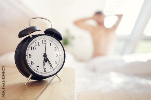 Alarm clock morning wake up time with man stretching on bed