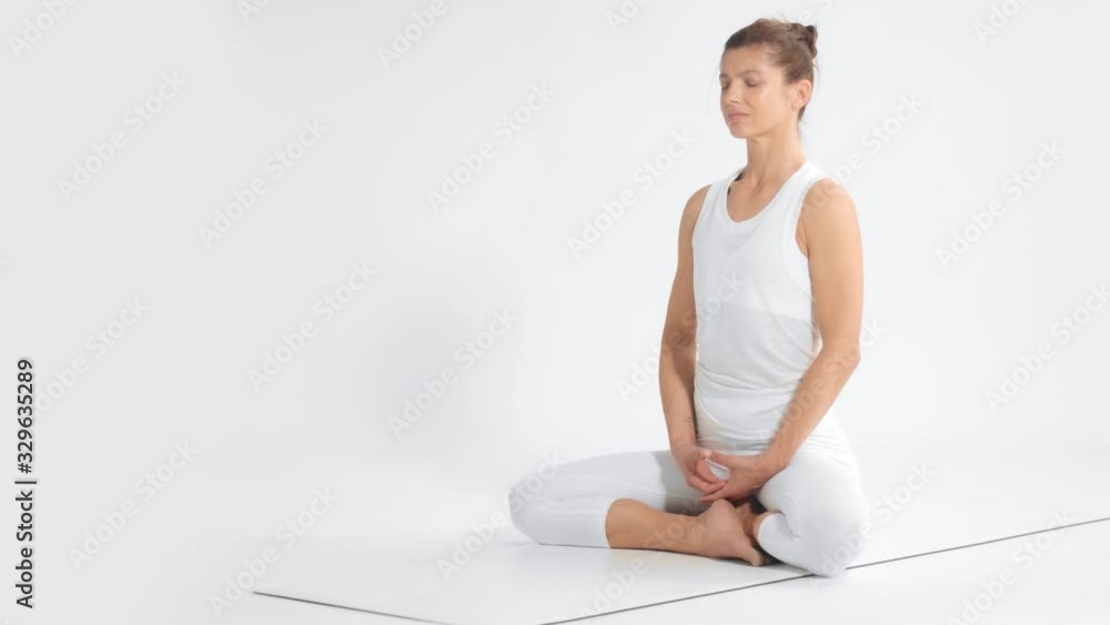 Senior woman in white space practice yoga sits in lotus position pan movement dolly Senior woman in white space practice yoga sits in lotus position pan movement dolly