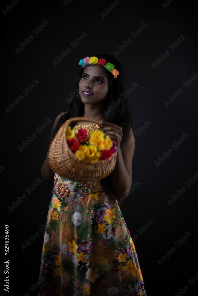Fashion portrait of young dark skinned Indian Bengali brunette girl in floral dress with floral head band taking flowers in front of black copy space studio background. Indian fashion photography. Fashion portrait of young dark skinned Indian Bengali brunette girl in floral dress with floral head band taking flowers in front of black copy space studio background. Indian fashion photography.