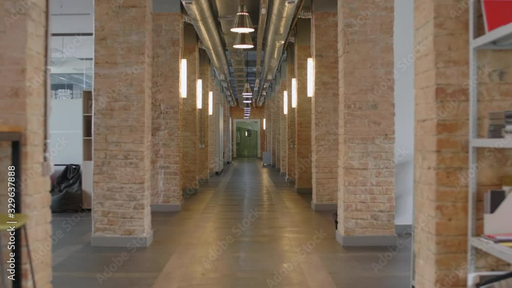 Zoom out shot of empty hallway with brick columns and lamps in modern loft office. There are comfortable bean bag chairs, shelves with stationery and chairs Zoom out shot of empty hallway with brick columns and lamps in modern loft office. There are comfortable bean bag chairs, shelves with stationery and chairs