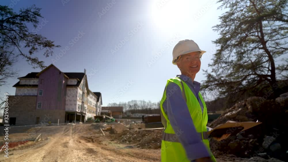 Wide angle extreme closeup of woman engineer architect walking towards camera on construction site and looking at camera and smiling. Wide angle extreme closeup of woman engineer architect walking towards camera on construction site and looking at camera and smiling.
