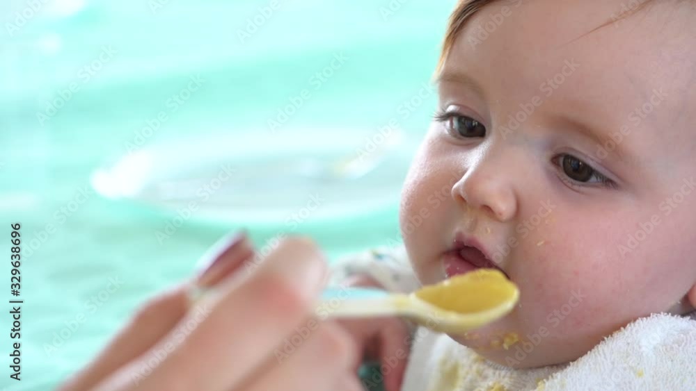 A mother's hand carrying a spoon full of baby food is twirled around just before it enters into the toddlers mouth, Close up shot slow motion A mother's hand carrying a spoon full of baby food is twirled around just before it enters into the toddlers mouth, Close up shot slow motion