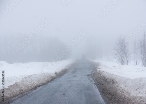 Rural asphalt road on foggy winter day, with truck in the distance