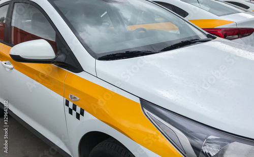 Close up side view of  yellow and white taxi car with checker, and the same taxi car near on parking