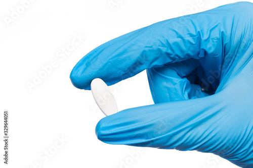 Surgeon's hand in a blue medical glove holds a pill blister isolated on white background