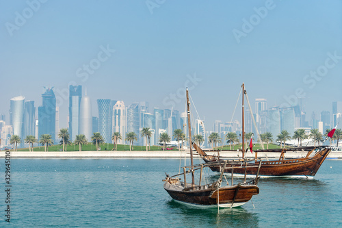 Retro historical boat with blurred panoramic view of modern skyline of Doha and green palms on background