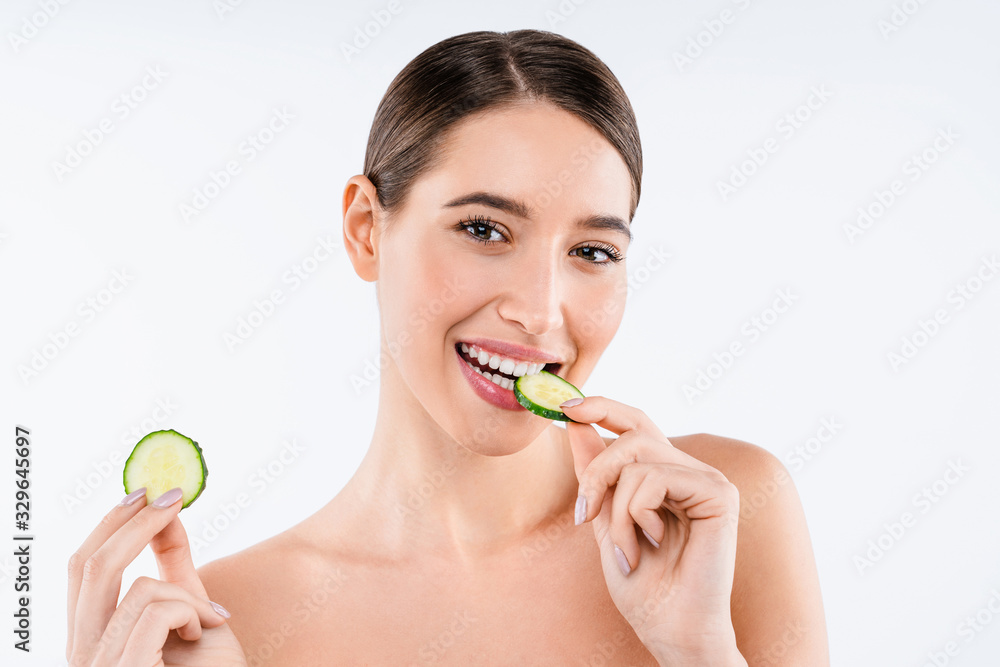 Beauty portrait of smiling young topless woman eating slice of cucumber standing isolated over white background Beauty portrait of smiling young topless woman eating slice of cucumber standing isolated over white background