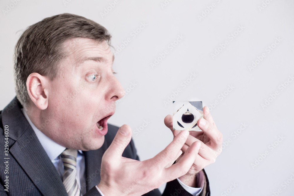 Fototapeta premium Nervous businessman in suit holds in hands drop of black oil of Brent brand, screams and shouts. Crystal cube. Crisis in financial market, falling and rising prices, quotes, changes in exchange rate