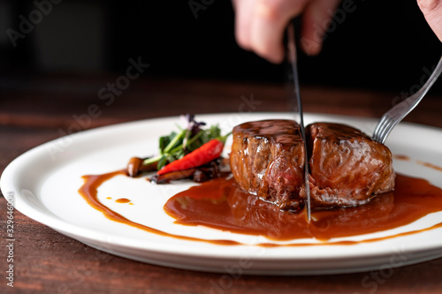 Beef tenderloin steak in demiglas sauce is cut with a knife on a white platter photo