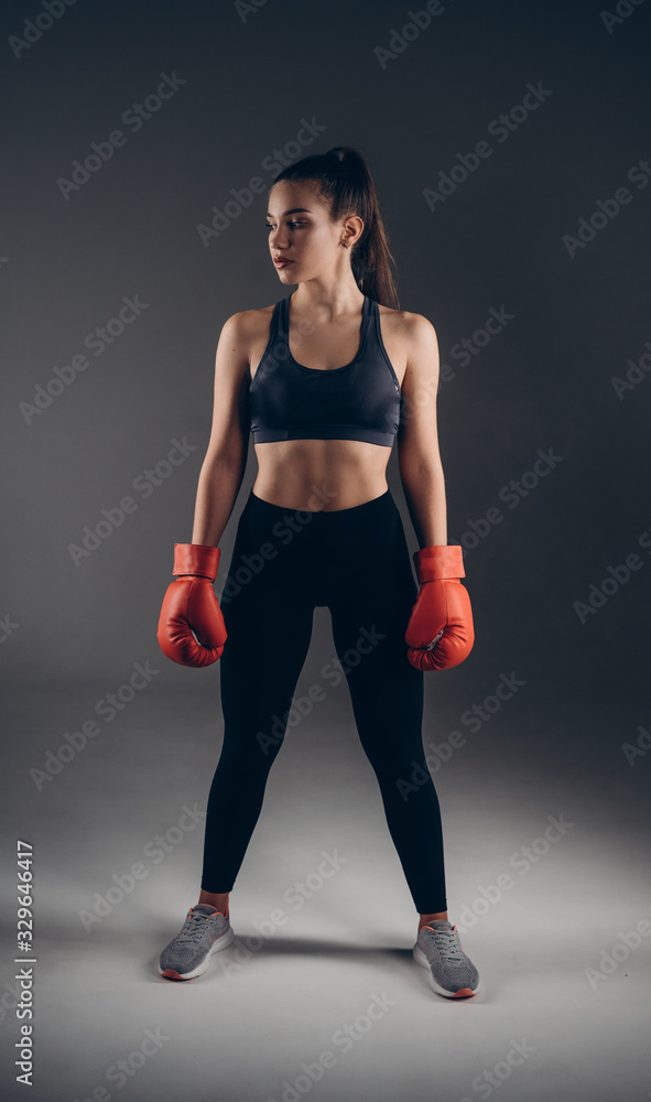 Full-leght Image of a beautiful young amazing sports fitness caucasian woman boxer posing isolated over gray background in red gloves. Full-leght Image of a beautiful young amazing sports fitness caucasian woman boxer posing isolated over gray background in red gloves.
