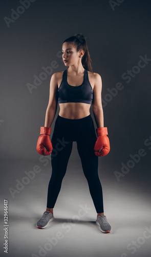 Full-leght Image of a beautiful young amazing sports fitness caucasian woman boxer posing isolated over gray background in red gloves. © Owl-vision-studio