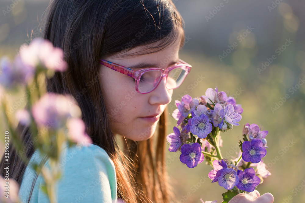 A girl is smelling flowers while on an outdoor hike.
