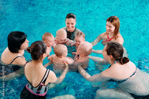 A group of mothers with their young children in a children's swimming class with a coach. © davit85