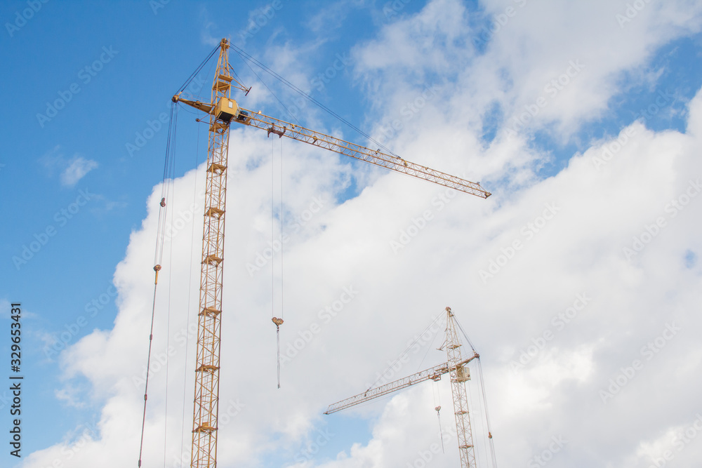 Two tower cranes against a blue sky with clouds Two tower cranes against a blue sky with clouds