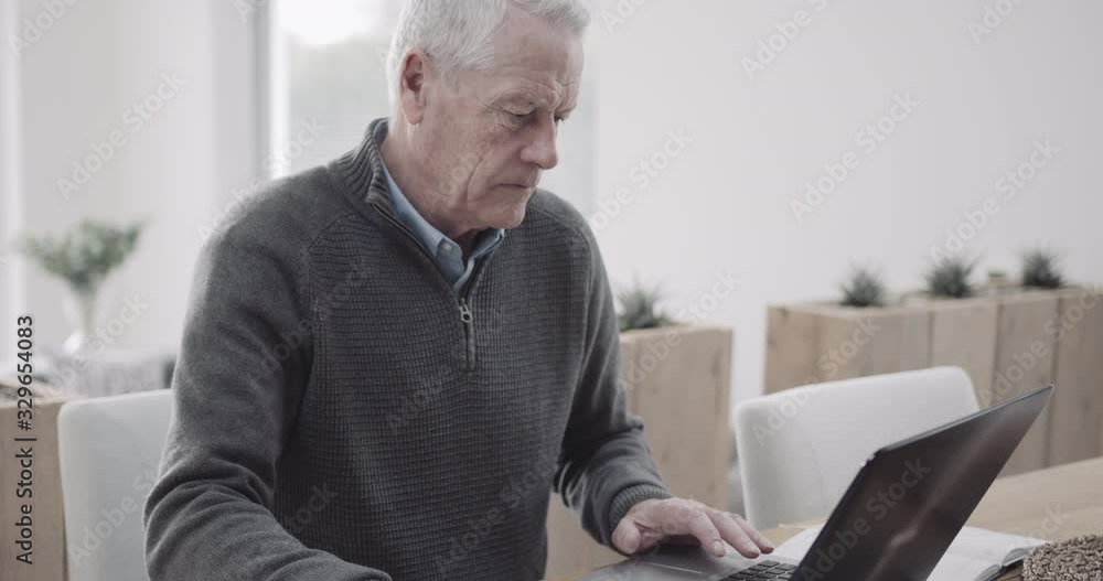 Senior adult male doing domestic finance on laptop at kitchen table, day in life Senior adult male doing domestic finance on laptop at kitchen table, day in life