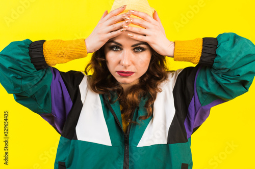 Modern beautiful girl in oversized sports jacket, hat and jeans, Billie Eilish style, back in the 90s, 2000s. Posing in the studio on a yellow background, strong funny emotions photo