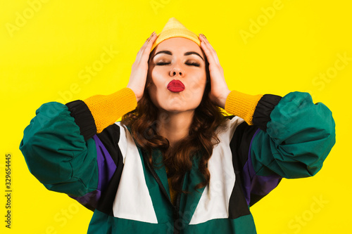 Modern beautiful girl in oversized sports jacket, hat and jeans, Billie Eilish style, back in the 90s, 2000s. Posing in the studio on a yellow background. photo