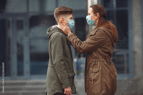 A boy and mother are wearing protective masks. The kid is sneezing and mother is helping him to wear a piece of protective equipment.