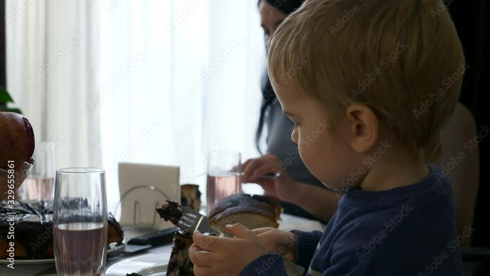 Cute Child Eats Vegan Chocolate Cherry Pie. Healthy food. On Blurred Background Young Mother Drinking Compote. Slow motion 0.5 speed 60 fps Cute Child Eats Vegan Chocolate Cherry Pie. Healthy food. On Blurred Background Young Mother Drinking Compote. Slow motion 0.5 speed 60 fps