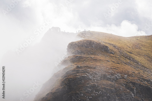 Silhouettes of five hillwalkers on the top of the Cobbler with rugged cliffs in deep fog. Dramatic Scottish landscape. photo