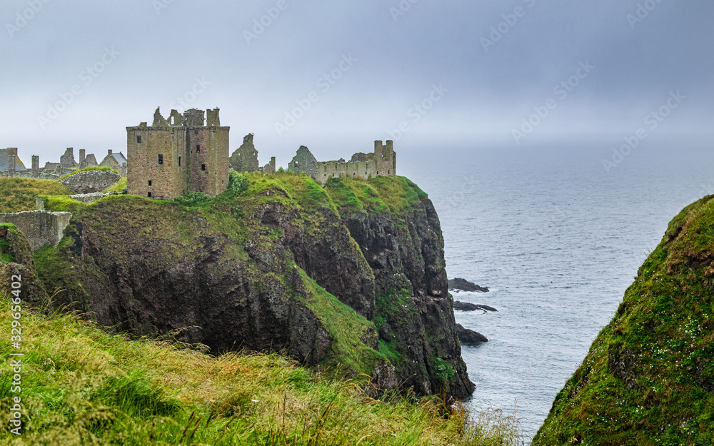 Dunnottar Castle ruins perched on the cliffs of Aberdeenshire coat, Scotland, on a foggy and rainy summer day.