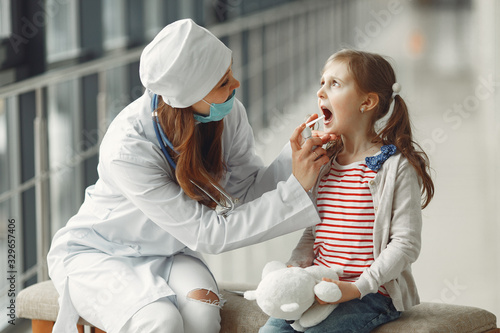 The doctor in a mask is sparing throat antiseptic for a child. photo