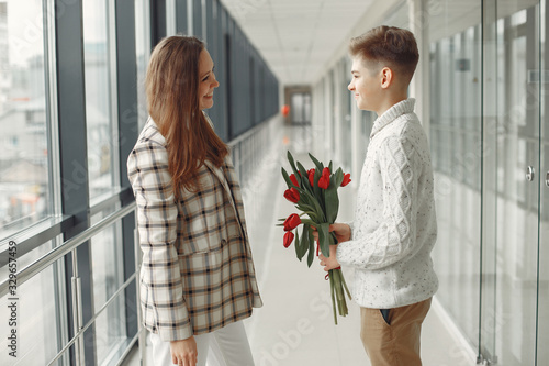 Son giving a mother a bunch of red tulips in amodern hall. photo