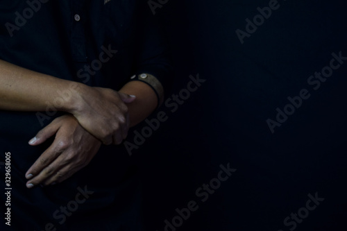 Young man praying with arms across posture. Islamic praying concept on black background. Selective focus on finger
