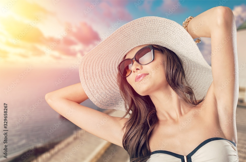 Beautiful young woman in sunglasses, hat and fashionable swimsuit