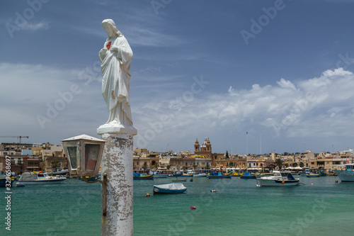 White religious icon statue on a post overlooking Marsaxlokk harbour © Elloria Voltan