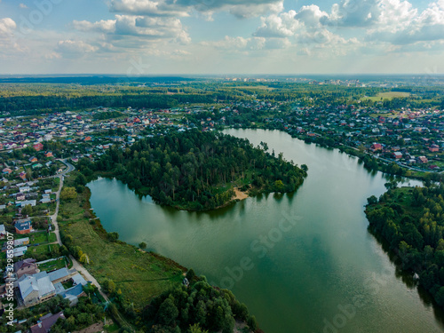 Green peninsula with coniferous trees on the river in the suburbs, against the backdrop of summer nature. Aerial photography