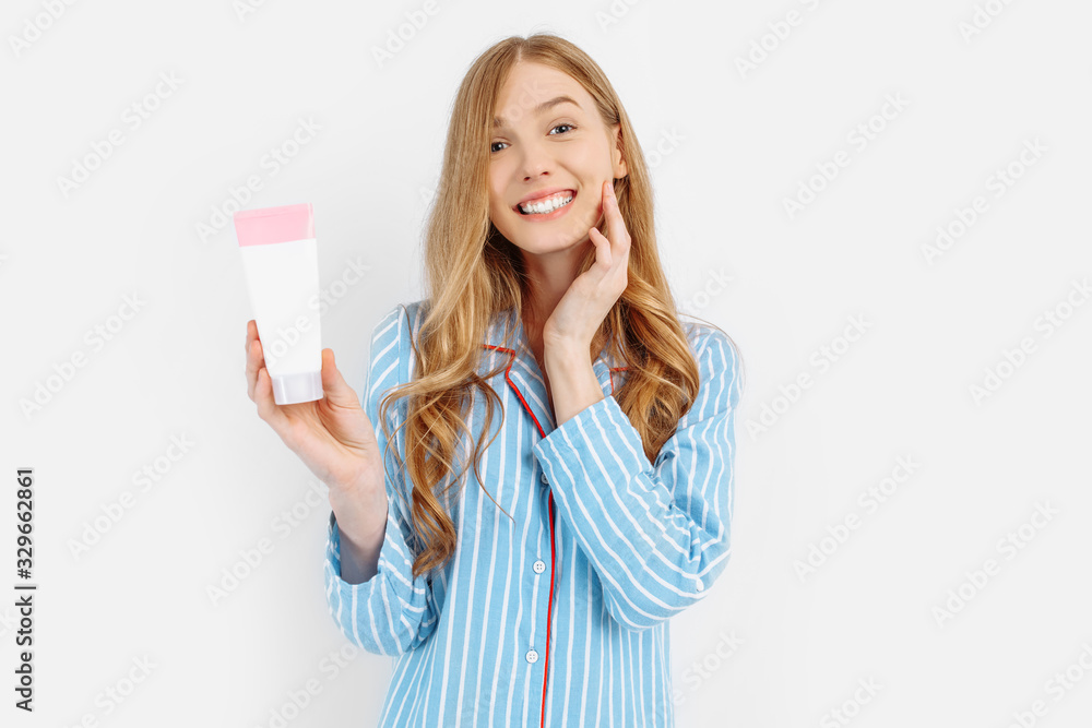 Portrait of happy beautiful young woman in pajamas standing isolated on white background applying face lotion Portrait of happy beautiful young woman in pajamas standing isolated on white background applying face lotion