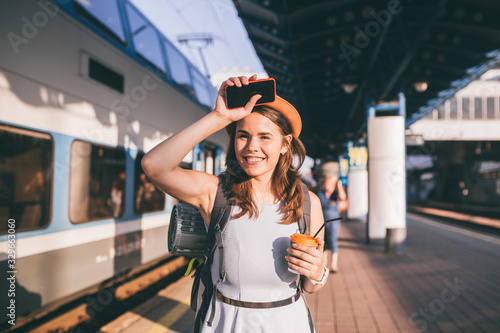 Tourism and travel in the summer. Vacations for the student. Work and travel. Caucasian young woman drinks coffee on the platform of the railway station against the background of the train
