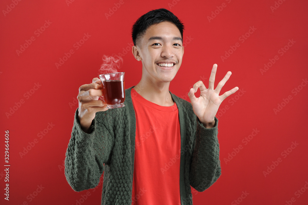 Happy Young Asian man smiling drink hot tea with finger okay sign Happy Young Asian man smiling drink hot tea with finger okay sign
