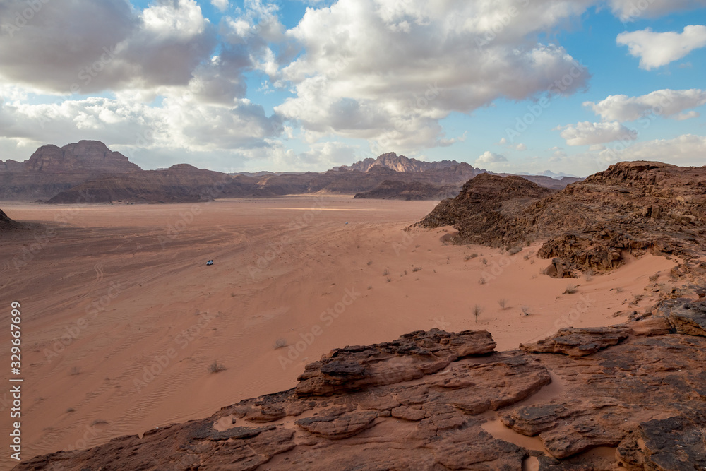 Kingdom of Jordan, Wadi Rum desert, sunny winter day scenery landscape with white puffy clouds and warm colors. Lovely travel photography. Beautiful desert could be explored on safari. Miniature car