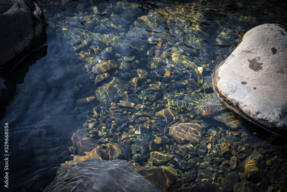Fototapeta premium summer sunshine creates beautiful patterns on river stones under water
