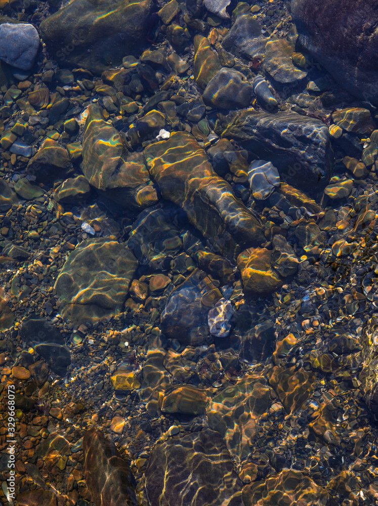summer sunshine creates beautiful patterns on river stones under water