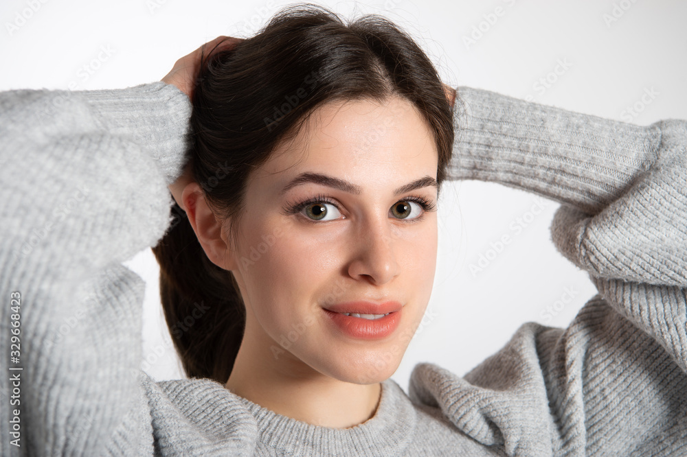Charming caucasian girl in grey sweater holding hands behind her head and looking at camera. Beautiful smiling female model with perfect makeup and graceful red lipstick... Charming caucasian girl in grey sweater holding hands behind her head and looking at camera. Beautiful smiling female model with perfect makeup and graceful red lipstick...