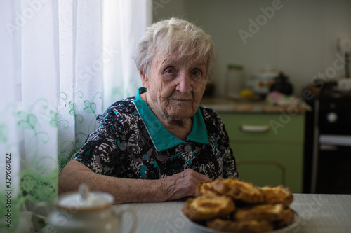 An Old woman drinking tea in the kitchen. Care for pensioners and the elderly.