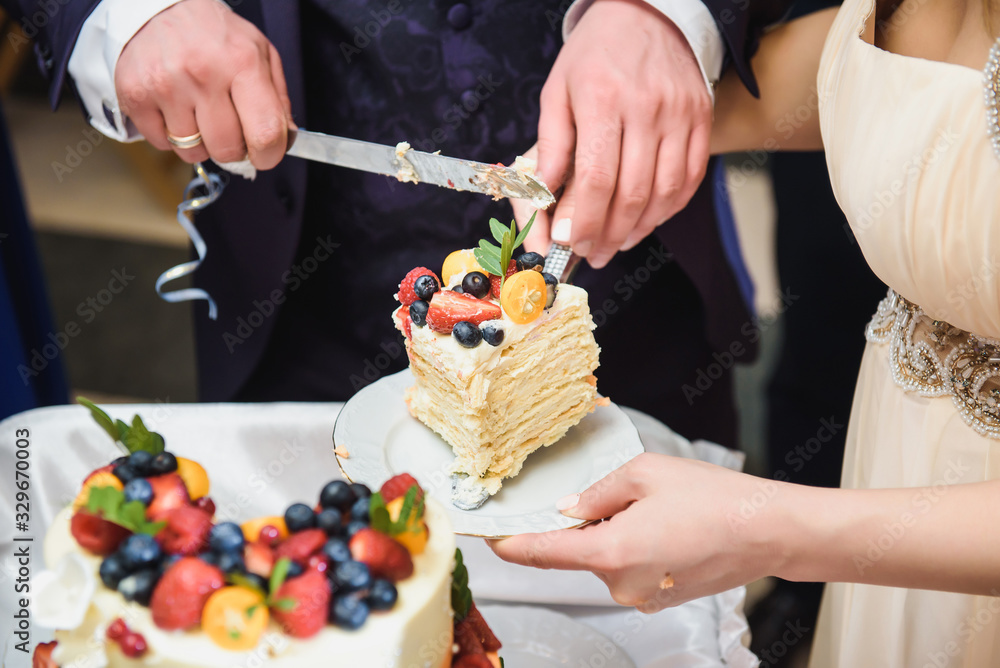 Bride and a groom is cutting their fruit rustic wedding cake on wedding banquet. Hands cut the cake with delicate pink flowers.