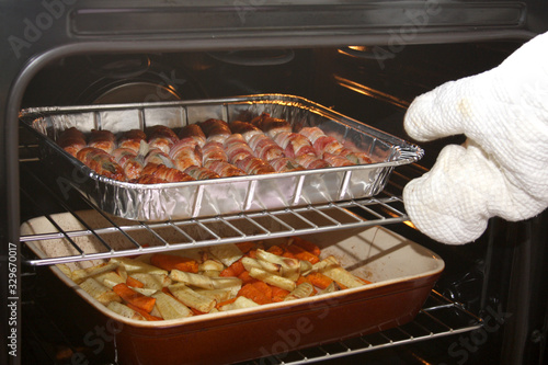 An oven full of sausages with bacon and roasting vegetables