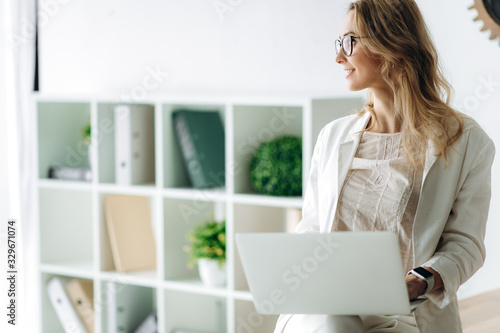 A young girl in a white suit with a laptop is sitting on a table and looking away