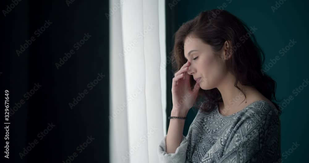 Side view of young thoughtful lady with curly hair dressed casually looking through window at home. Pretty woman feeling loneliness and sadness during leisure time. Side view of young thoughtful lady with curly hair dressed casually looking through window at home. Pretty woman feeling loneliness and sadness during leisure time.
