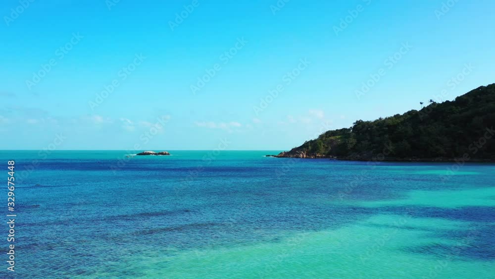 Blue azure sea water washing beautiful rocky coastline of tropical island at sunrise with bright sky Blue azure sea water washing beautiful rocky coastline of tropical island at sunrise with bright sky