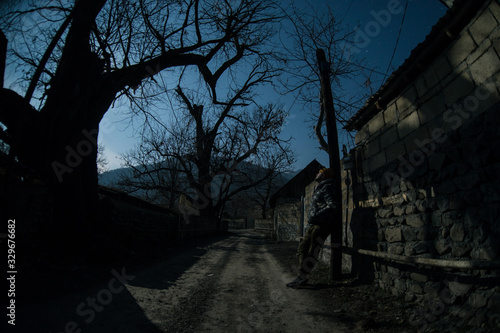 Full moon over quiet village at night. Beautiful night landscape of mountain village under the moonlight. Silhouette of person standing in the dark. Selective focus.