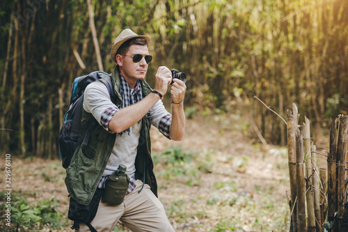 Portrait of male photographer with vintage camera taking in bamboo forest, man traveler and backpack hiking outdoors