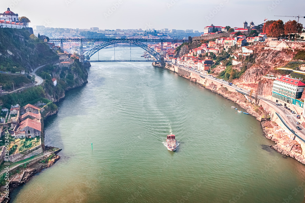 Travel Ideas. Traditional Red Tourist Travel Boat Floating in Porto City Across The Douro River in Portugal. Cityscape with Red Rooftops in Background